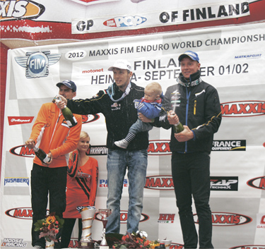 Enduro MM-turniiril võidukas Aigar Leok pühapäeval Soomes Heinolas pjedestaali kõrgeimal astmel koos 11-kuuse poja Lucasega, vasakul teiseks tulnud prantslane Christophe Nambotin ja paremal kolmas mees, rootslane Joakim Ljunggren. Foto: AIVAR LEOK
