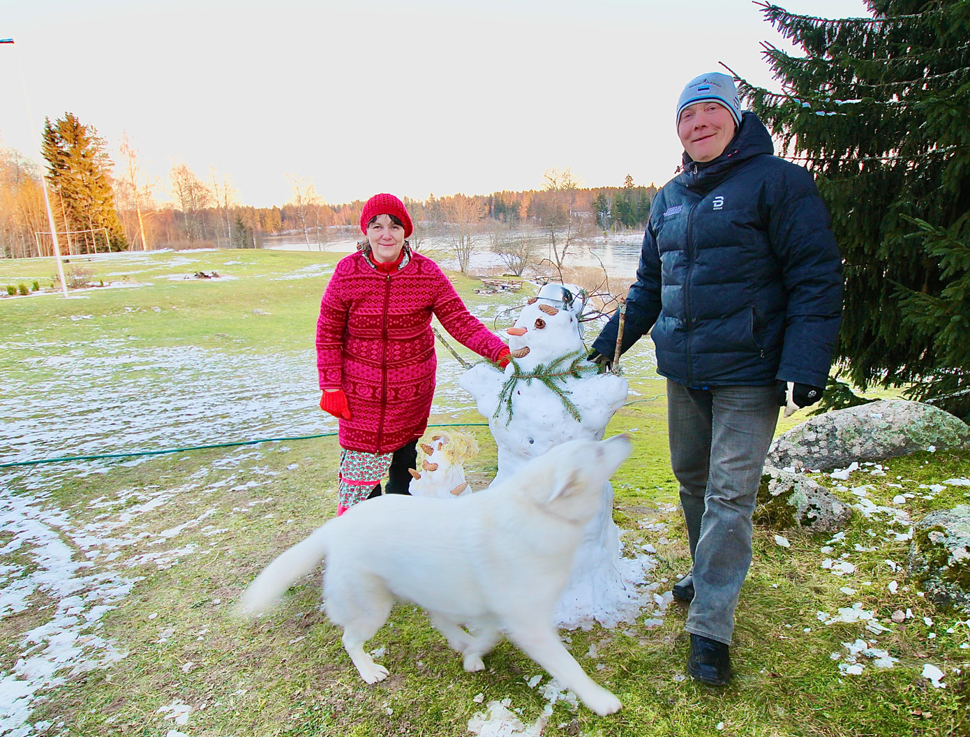 Vaskna jõulutalu perenaine Margit ja peremees Ahti Utsal tunnevad rõõmu lähenevatest jõuludest ja talvest ning tutvustavad õuel lumest Käbimemme ja Oksamemme. Pererahva heast tujust on nakatunud ka nelja-aastane koer nimega Lumi. Taamal päiksekullas jääkaane all Vaskna järv. FOTO: Kalev Annom