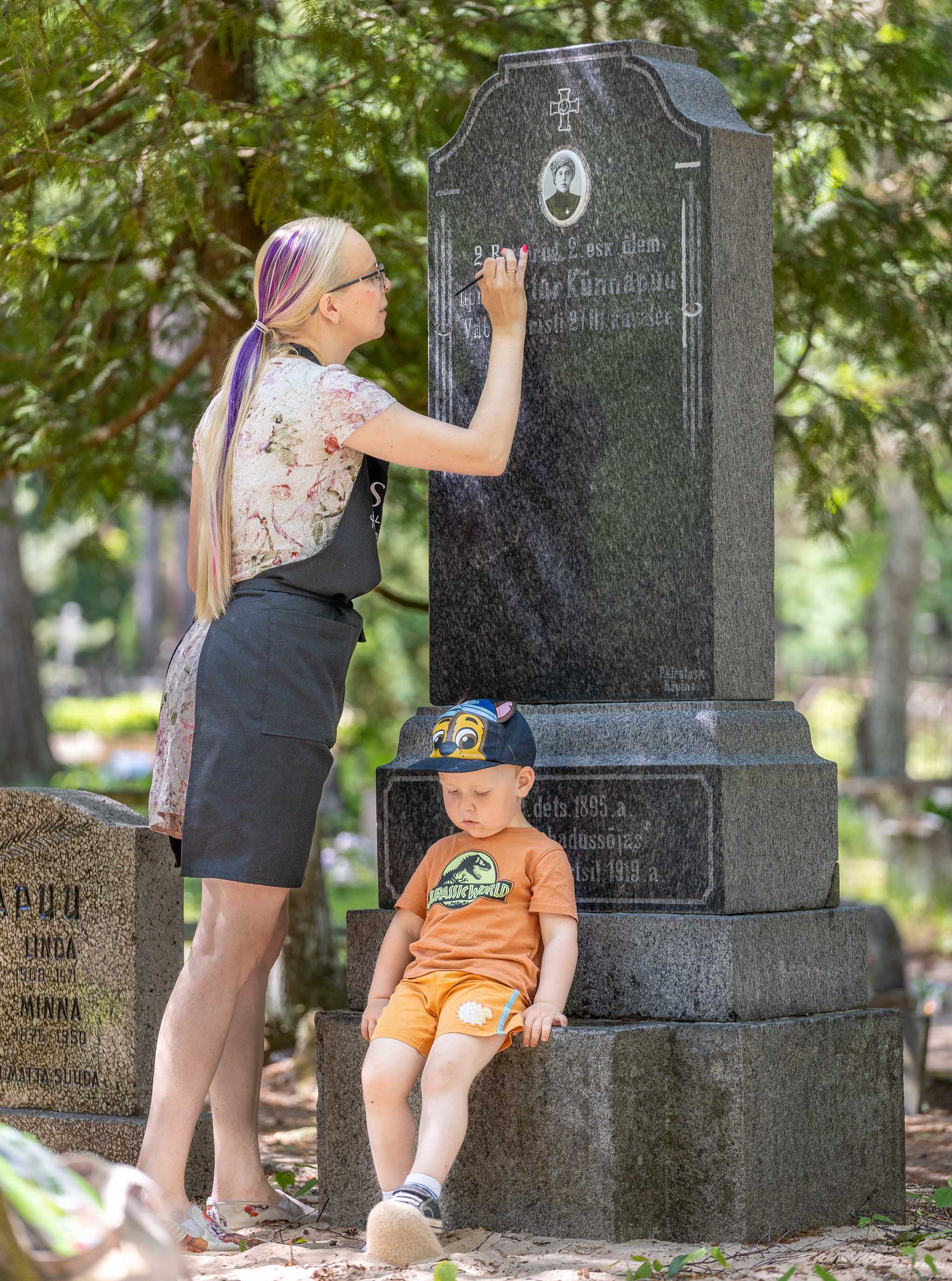 Crafteri üks omanik Regina Vildo koos peagi kolmeaastaseks saava poja Ralfiga neljapäeva lõuna ajal Võru linnakalmistul mineraalvärviga Fusion hauakividel olevat teksti taastamas.   Foto: AIGAR NAGEL